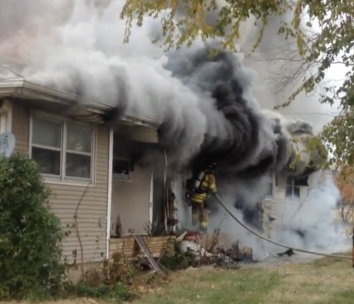 House on fire, with firefighters on front porch putting the fire out. 